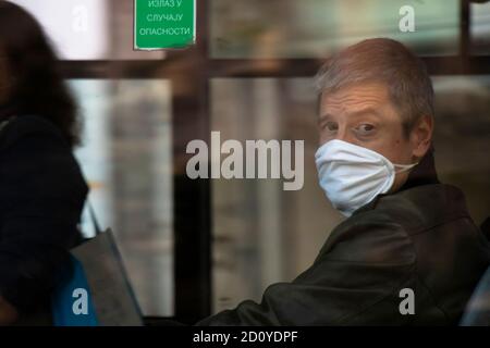 Belgrado, Serbia - 02 ottobre 2020: Uomo maturo che indossa una maschera facciale mentre si guida su un sedile della finestra in un autobus, attraverso la finestra Foto Stock