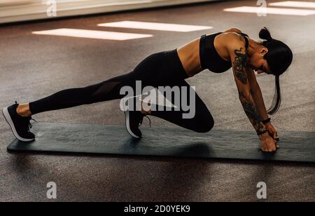 Vista laterale della femmina sottile in abbigliamento sportivo che si esercita sul tappetino e allungare le gambe prima di allenarsi Foto Stock