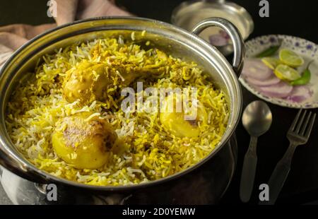 Delizioso e piccante biryani di pollo fatto in casa in ciotola tradizionale con raita e insalata su fondo nero Foto Stock