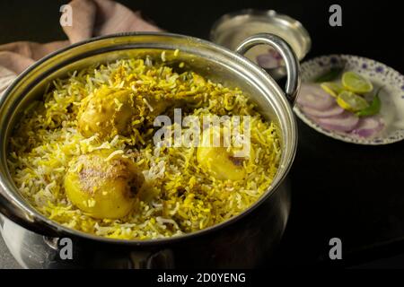 Delizioso e piccante biryani di pollo fatto in casa in ciotola tradizionale con raita e insalata su fondo nero Foto Stock