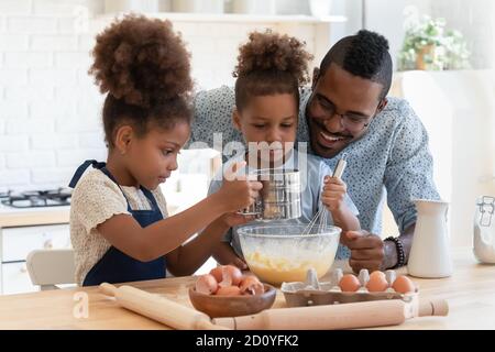 Felice uomo afroamericano che prepara l'impasto con i bambini. Foto Stock