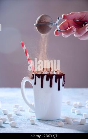 Bevanda calda di Natale. Coppa bianca di cacao o cioccolato con marshmallows e cacao in polvere volante su sfondo chiaro. Foto Stock