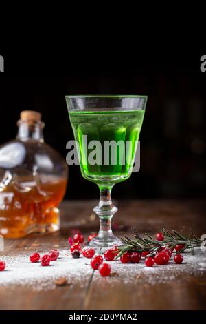 Cocktail verde sulla base di assenzio in un elegante vintage vetro su di un legno marrone. sfondo dello zucchero bianco e mirtilli sono sparsi nei dintorni Foto Stock