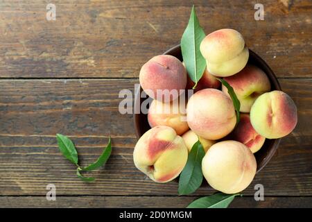 Pesche mature con foglie in una ciotola di argilla su un tavolo di legno. Raccolto fresco. Vista dall'alto. Foto Stock