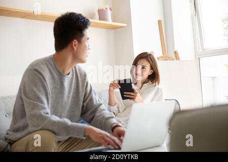 felice e rilassata giovane coppia asiatica che chiacchiera mentre si soggiorna a casa Foto Stock