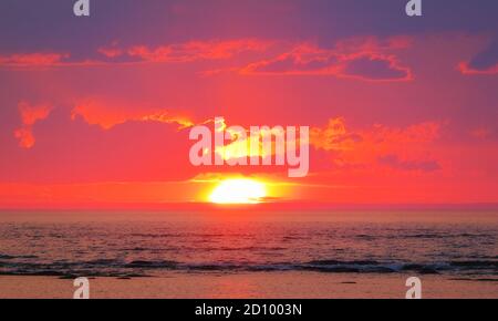 Luminoso arancio tramonto luce sul mare e nuvole sopra orizzonte Foto Stock