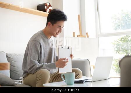 felice e sorridente giovane dirigente d'azienda asiatica che lavora da casa incontro con colleghi o clienti tramite videochiamata Foto Stock