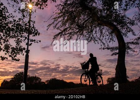 Pedalando come il sole tramonta in una giornata autunnale con una luce stradale accesa per facilitare la visibilità Foto Stock