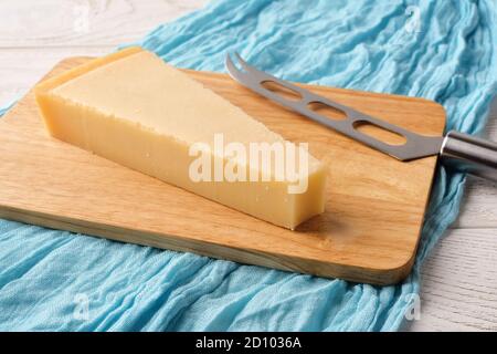 Cuneo triangolare di formaggio tradizionale italiano duro Grana Padano o Parmigiano e coltello formaggio su un boad di taglio legno su tavola di legno bianco. Vista frontale Foto Stock