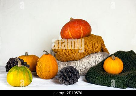Coni di abete e zucche con maglie a maglia su fondo bianco di legno. Concetto di vacanza autunno e inverno. Foto Stock