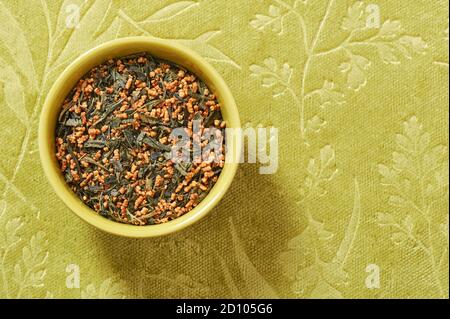 Genmaicha giapponese, tè verde con riso arrosto, una ciotola su sfondo tessile verde con uno spazio copia Foto Stock