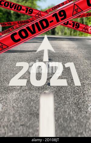 Strada asfaltata con segnaletica stradale, nastri di avvertimento gialli etichettati COVID-19 e numero 2021 dell'anno. Con COVID-19 all'anno 2021 Foto Stock