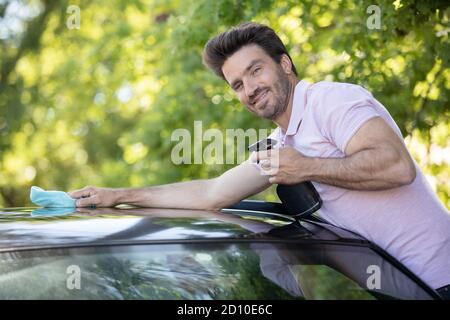 giovane uomo che pulisce il tetto di vetro sulla sua auto Foto Stock
