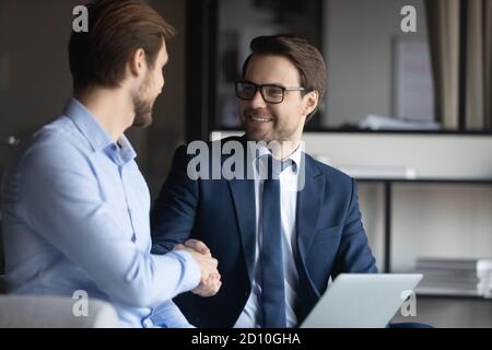 Uomo d'affari sorridente in occhiali e vestito scuotendo le mani con il partner. Foto Stock