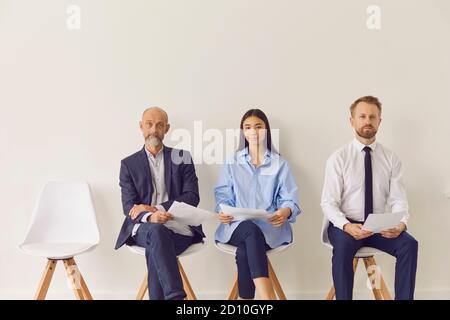 Tre candidati multirazziali di diverse età seduti su sedie in attesa per un colloquio di lavoro Foto Stock