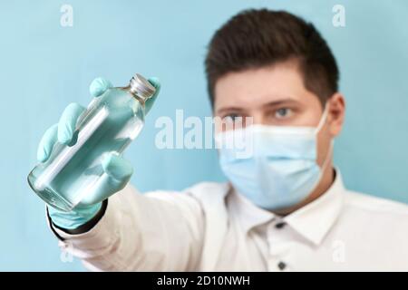 l'uomo di concetto del coronavirus in maschera medica guarda la bottiglia sopra sfondo blu Foto Stock