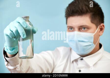 l'uomo di concetto del coronavirus in maschera medica guarda la bottiglia sopra sfondo blu Foto Stock