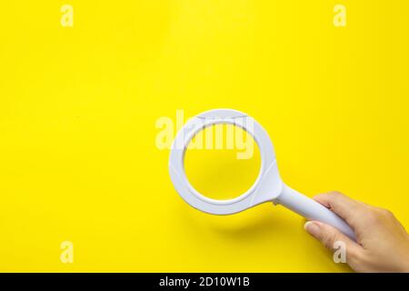 Primo piano tenendo la lente di ingrandimento con la mano su sfondo giallo. Gestione SEO Foto Stock