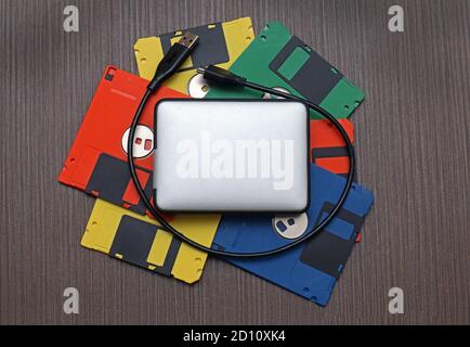 Pila di floppy disk retrò colorati con disco rigido esterno moderno in alto Foto Stock