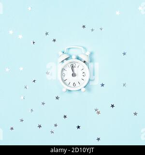 Sveglia in stile vintage bianco che mostra cinque minuti a sinistra fino a mezzanotte su sfondo blu con sequine di stelle d'argento. Avvento del nuovo anno. Foto Stock