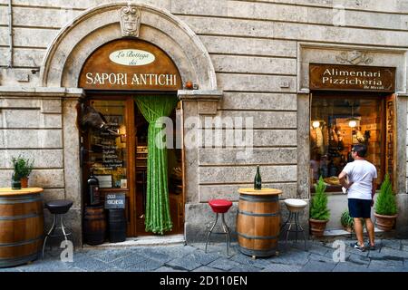 Esterno di un negozio di alimentari che vende prodotti tipici toscani e vino nel centro storico di Siena con un turista da dietro in estate, Toscana, Italia Foto Stock