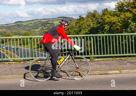 Ciclismo maschile equitazione Boardman squadra sport bici da strada sulla strada di campagna che attraversa il ponte autostradale nella rurale Lancashire, Regno Unito Foto Stock