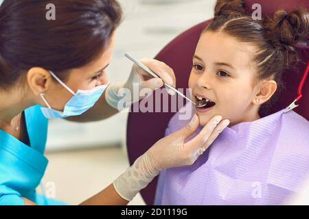 Donna dentista che esamina sorridente bambina ragazze denti con specchio in clinica dentale Foto Stock
