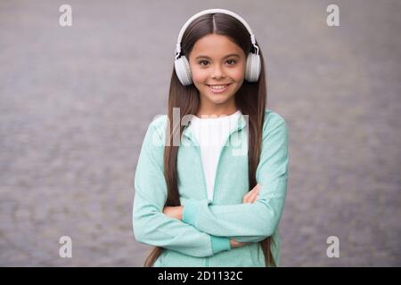 un bambino allegro indossa auricolari con canzone musicale all'aperto godendo della melodia, di nuovo a scuola. Foto Stock
