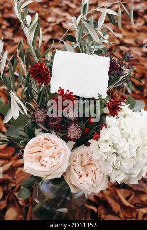 Matrimonio d'autunno, scena di mockup di compleanno. Bouquet floreale con rami d'ulivo, mamme, idrangea e fiori rosa rosa con carta booton bianca. Sfocato Foto Stock