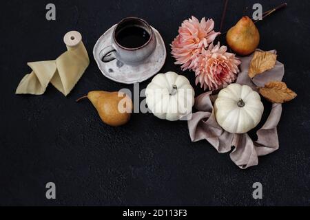 Composizione autunno natura morta. Tazza di caffè, pera e zucche bianche con fiori rosa di dahlia su sfondo nero. Moody caduta Foto Stock