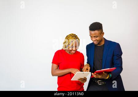 un giovane bell'uomo d'affari africano che ha messo il suo collega attraverso as le spiega che cosa è nel libro lui tiene mentre aziona il suo tablet Foto Stock