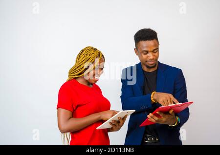 un giovane bell'uomo d'affari africano che ha messo il suo collega attraverso as le spiega che cosa è nel libro lui tiene mentre aziona il suo tablet Foto Stock