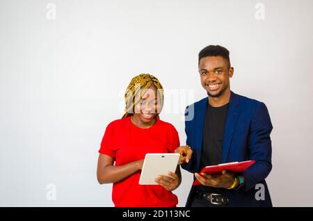 un giovane bell'uomo d'affari africano che ha messo il suo collega attraverso as le spiega che cosa è nel libro lui tiene mentre aziona il suo tablet Foto Stock