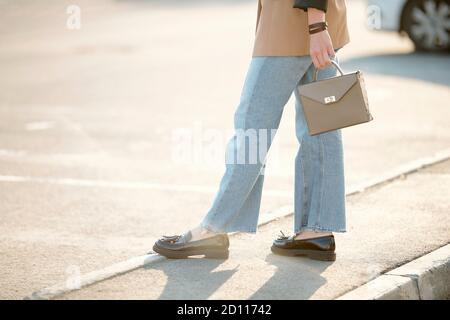 Sezione bassa di giovane donna elegante in scarpe nere, jeans blu e giacca marrone Foto Stock