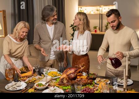Felici i membri giovani e maturi della famiglia che servono il tavolo del Ringraziamento per cena Foto Stock