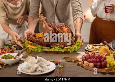 Mani di uomo maturo mettendo vassoio con grande arrosto fatto in casa turchia sul tavolo Foto Stock