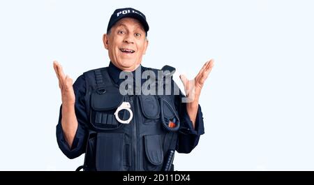 Uomo anziano bello che indossa uniforme della polizia celebrando la vittoria con felice sorriso e espressione vincente con le mani sollevate Foto Stock