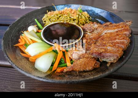 Piatto asiatico con anatra arrosto, verdure, tagliatelle e salsa teriyaki in una ciotola piatta su un tavolo di legno, fuoco selezionato, profondità di campo stretta Foto Stock