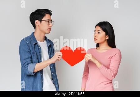 Coppia asiatica sconvolta che si guarda l'un l'altro e tiene il cuore Foto Stock