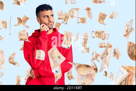 Giovane uomo ispanico che indossa abiti casual faccia seria pensare alla domanda con la mano sul mento, pensieroso circa idea confusa Foto Stock