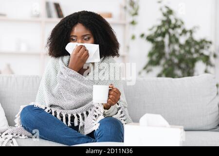 Donna afro malata avvolta in coperta soffiando il naso che corre Foto Stock