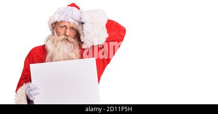 Vecchio uomo anziano con capelli grigi e barba lunga che indossa il costume di babbo natale che tiene banner stressato e frustrato con la mano sulla testa, sorpreso e arrabbiato Foto Stock