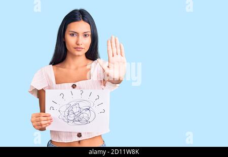 Giovane bella ragazza latina che tiene il tiraggio con la mano aperta facendo segno di stop con espressione seria e sicura, gesto di difesa Foto Stock