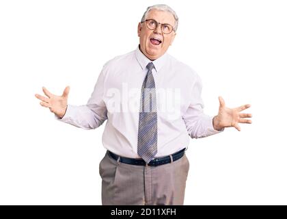 Uomo anziano con capelli grigi che indossa abiti da lavoro pazzo e pazzo gridando e urlando con espressione aggressiva e braccia sollevato. Concetto di frustrazione. Foto Stock
