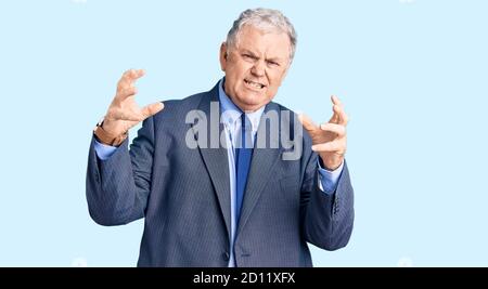 Uomo anziano con capelli grigi che indossa una giacca da lavoro gridando frustrato con rabbia, mani che cercano di strangolare, urlando pazzo Foto Stock
