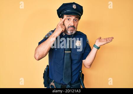 Uomo ispanico di mezza età che indossa uniforme della polizia confuso e infastidito con palma aperta che mostra lo spazio di copia e che punta il dito verso la fronte. Pensi a questo proposito. Foto Stock