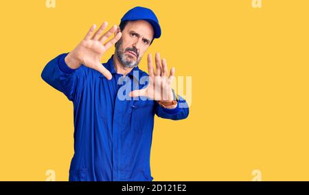 Bell'uomo di mezza età che indossa uniforme meccanica che fa cornice usando le mani palmi e dita, prospettiva della fotocamera Foto Stock