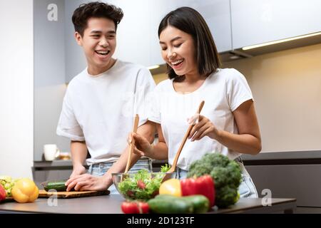 Happy Korean Couple Cooking e Laughing che preparano la cena a casa Foto Stock