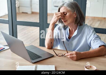Overlavored vecchia signora stanca che tiene gli occhiali che sente mal di testa dopo il lavoro del calcolatore. Foto Stock