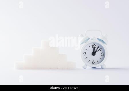 Pila ascendente di cubi di zucchero grafico e sveglia, studio girato isolato su sfondo bianco, salute elevato rischio di sangue di diabete concetto Foto Stock